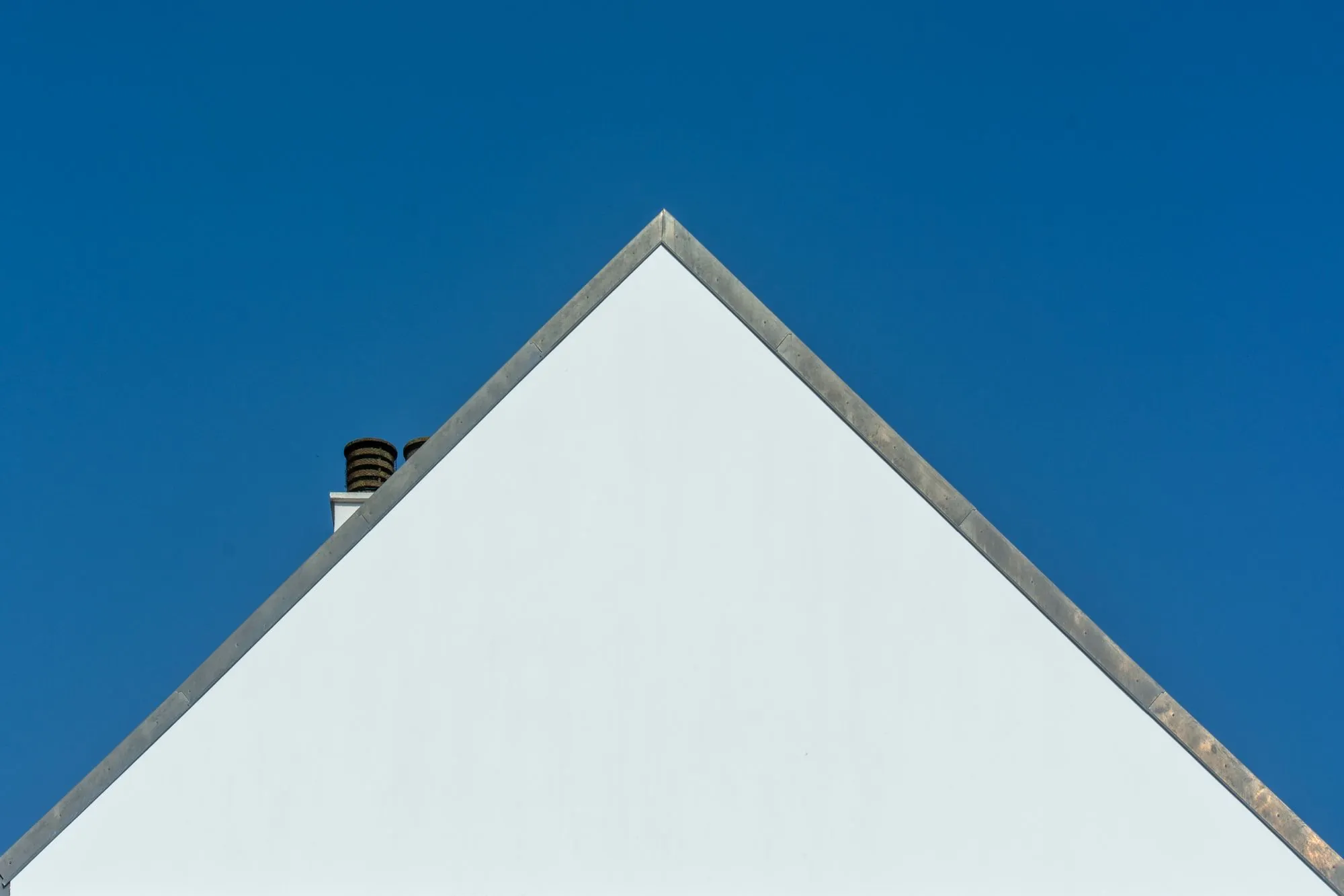 The gable end of a white house meeting a clear sky along the roofline
