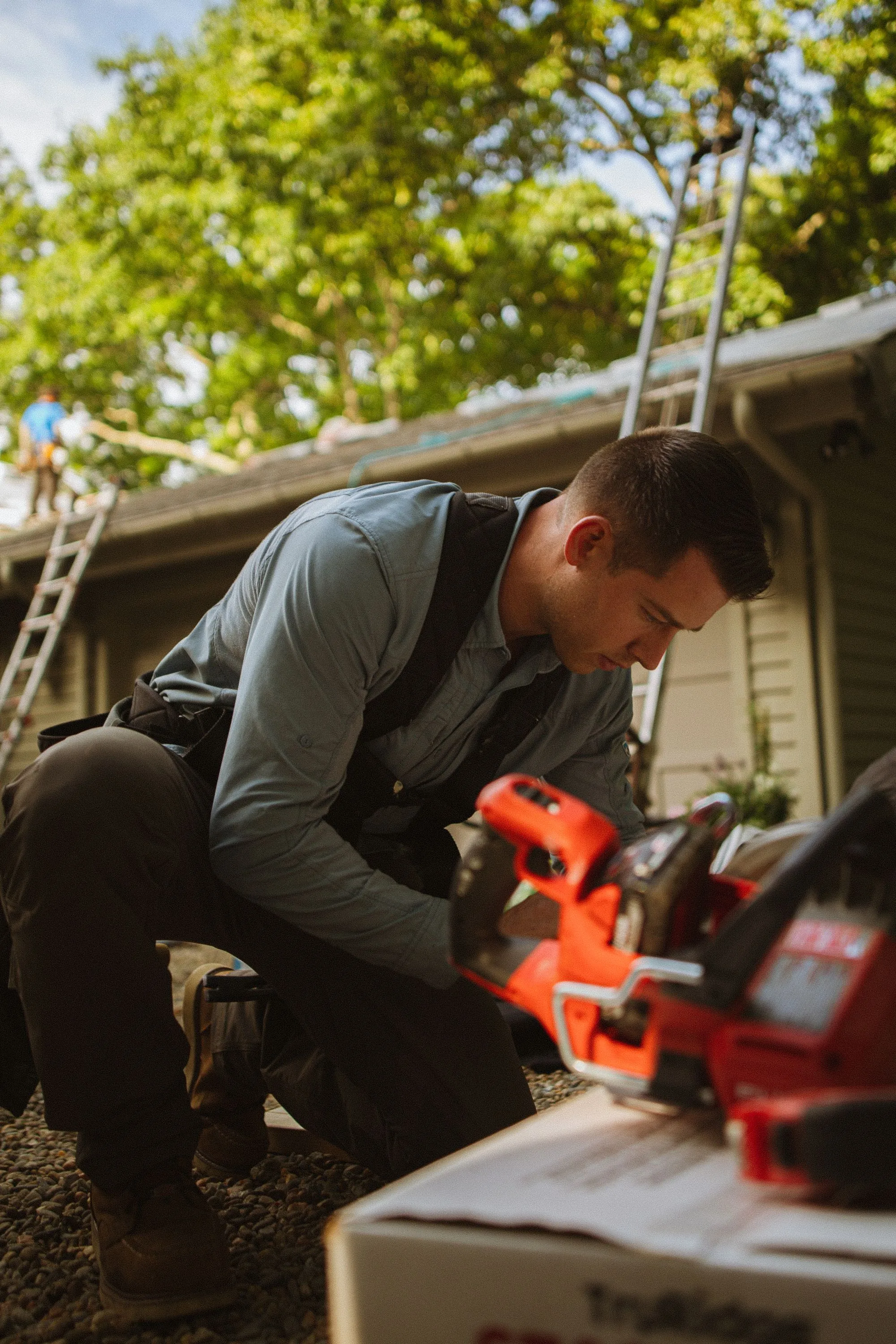 A roofer crouching beside a ladder with his tools, checking work on a house