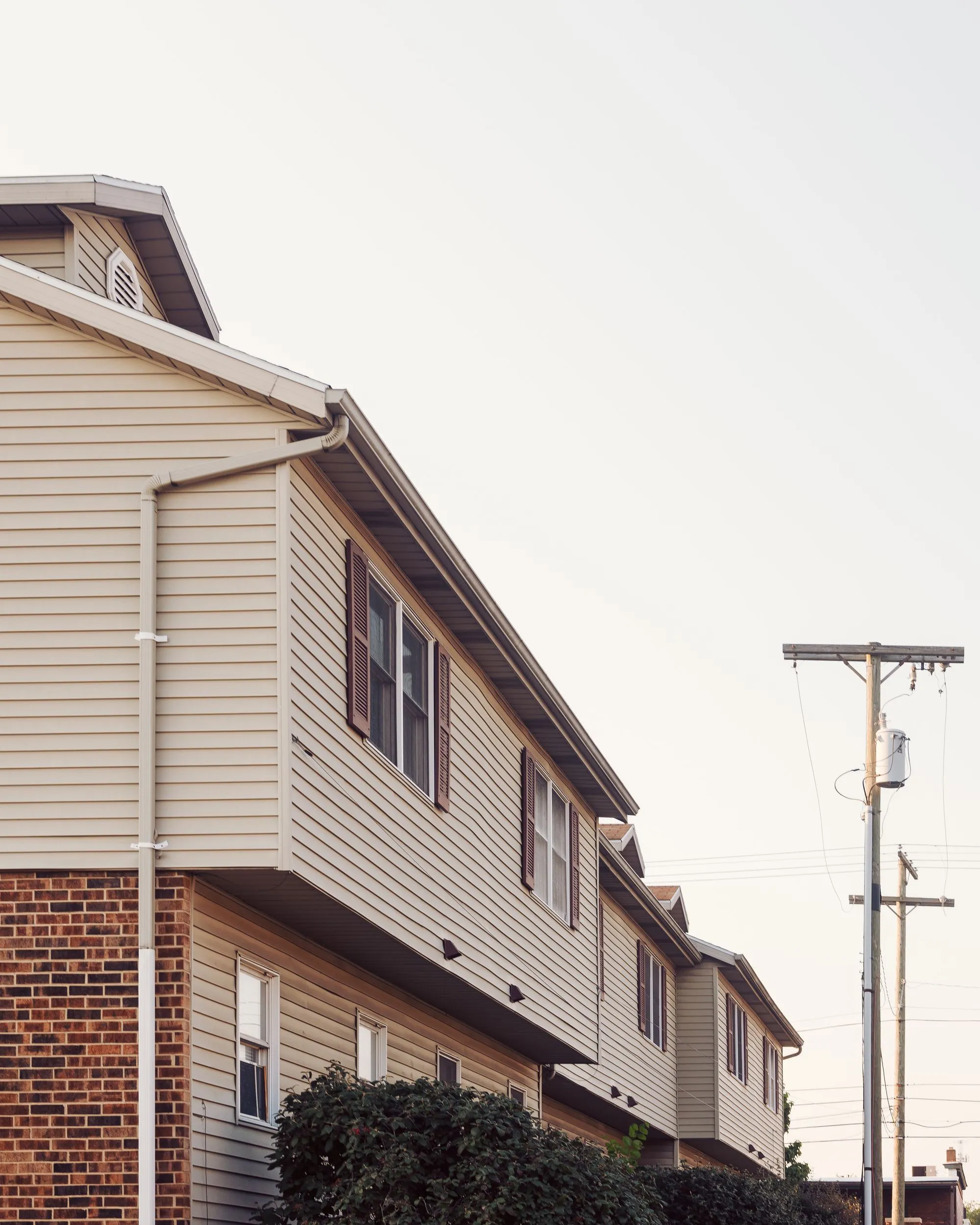 The side elevation of a two-storey house, siding and a shingled roof against a pale sky