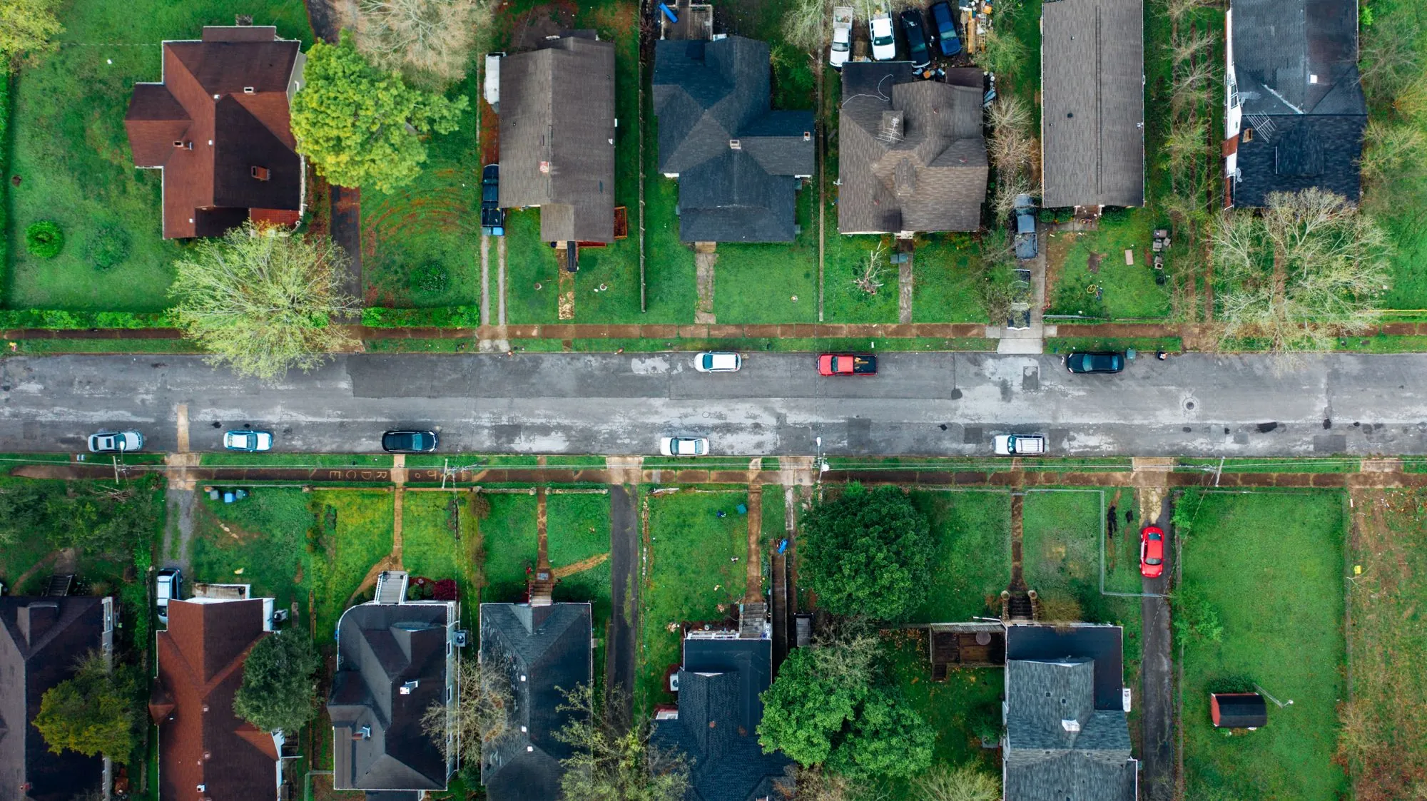 An overhead view of a residential street, rooftops and back gardens in a line