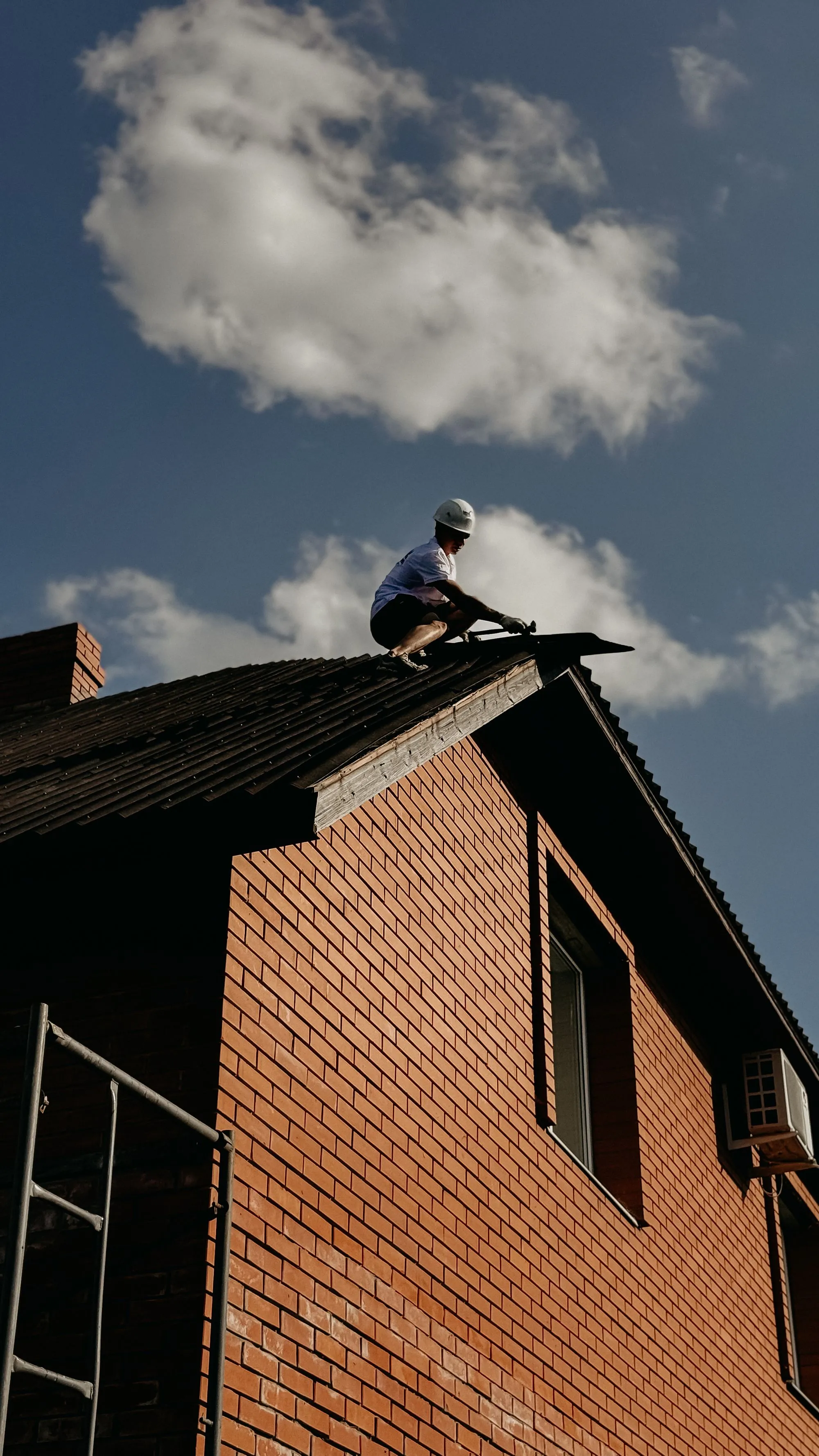 A roofer silhouetted against the sky as he works along the ridge of a brick house