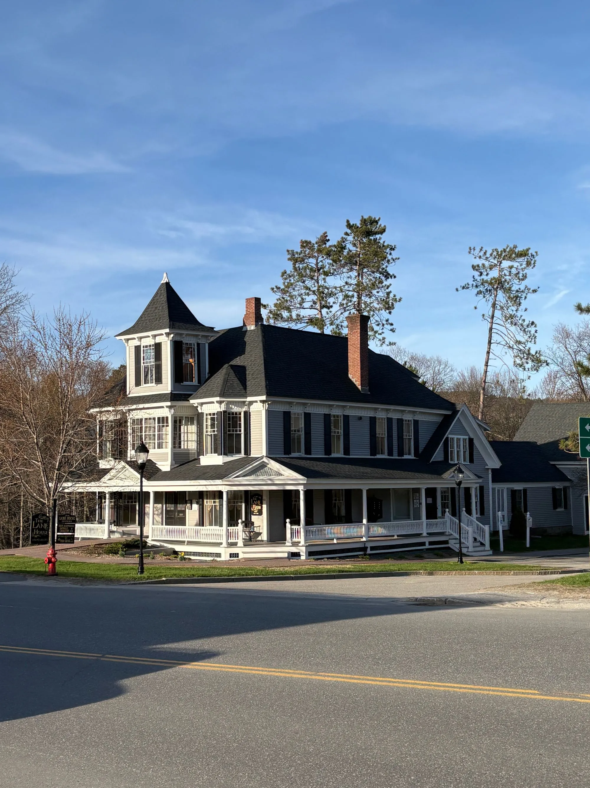 A white clapboard house with a wrap-around porch and a steep dark roof